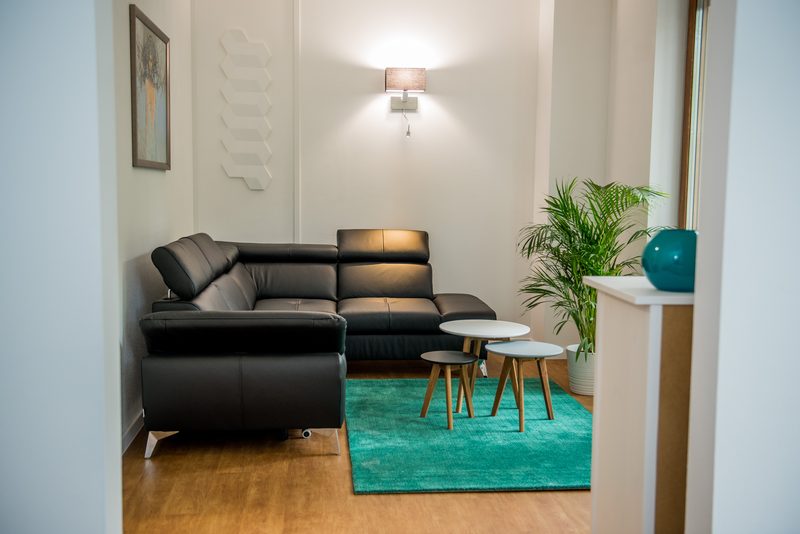 The apartment living room: a corner sofa, side tables and a green rug