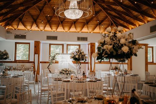 The Kryształowa hall with white chairs and tall bouquets, under the timber ceiling