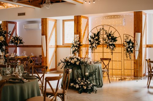 A floral arch behind the couple's table, against a curtain of lights