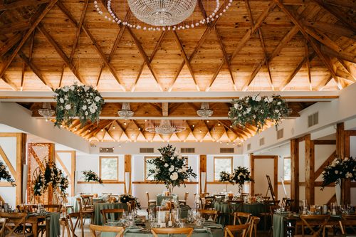 The timber ceiling of the Kryształowa hall with hanging floral arrangements, tables in sage green