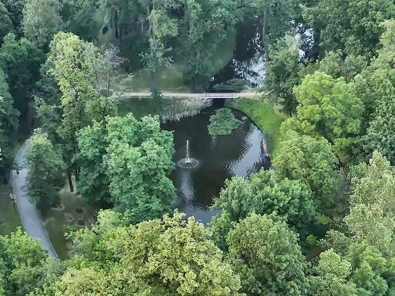 Szwajcaria Park from the air: a pond with a fountain and a stone bridge