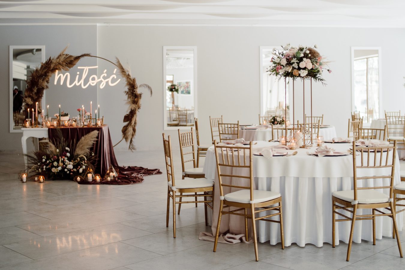 A light banquet hall with round tables and a glazed wall opening onto the park