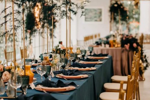 A long table laid in navy, with copper chargers and greenery above it